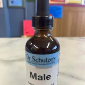 A bottle of Dr. Schulze’s Male (2 fl oz / 60 mL) with a dropper cap rests on a marble counter; its label states "Boosts Sexual Performance," is an herbal supplement, and features vegan and organic ingredients.