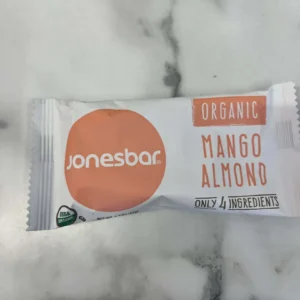A Jonesbar Organic Bar – Mango Almond, featuring white and orange packaging and just 4 ingredients, rests on a marble surface—a perfect vegan treat.