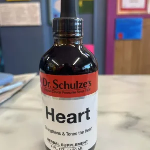 A bottle of Dr. Schulze's Heart herbal supplement with a dropper cap rests on a marble surface, labeled to support heart health.