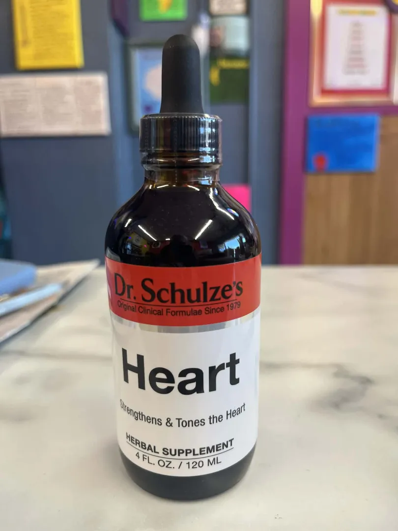 A bottle of Dr. Schulze's Heart herbal supplement with a dropper cap rests on a marble surface, labeled to support heart health.