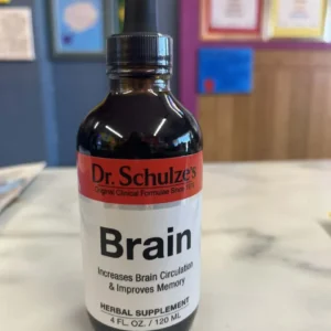 A bottle of Dr. Schulze's Brain organic herbal supplement with a dropper cap, which claims to boost brain circulation and memory, is displayed on a marble surface.