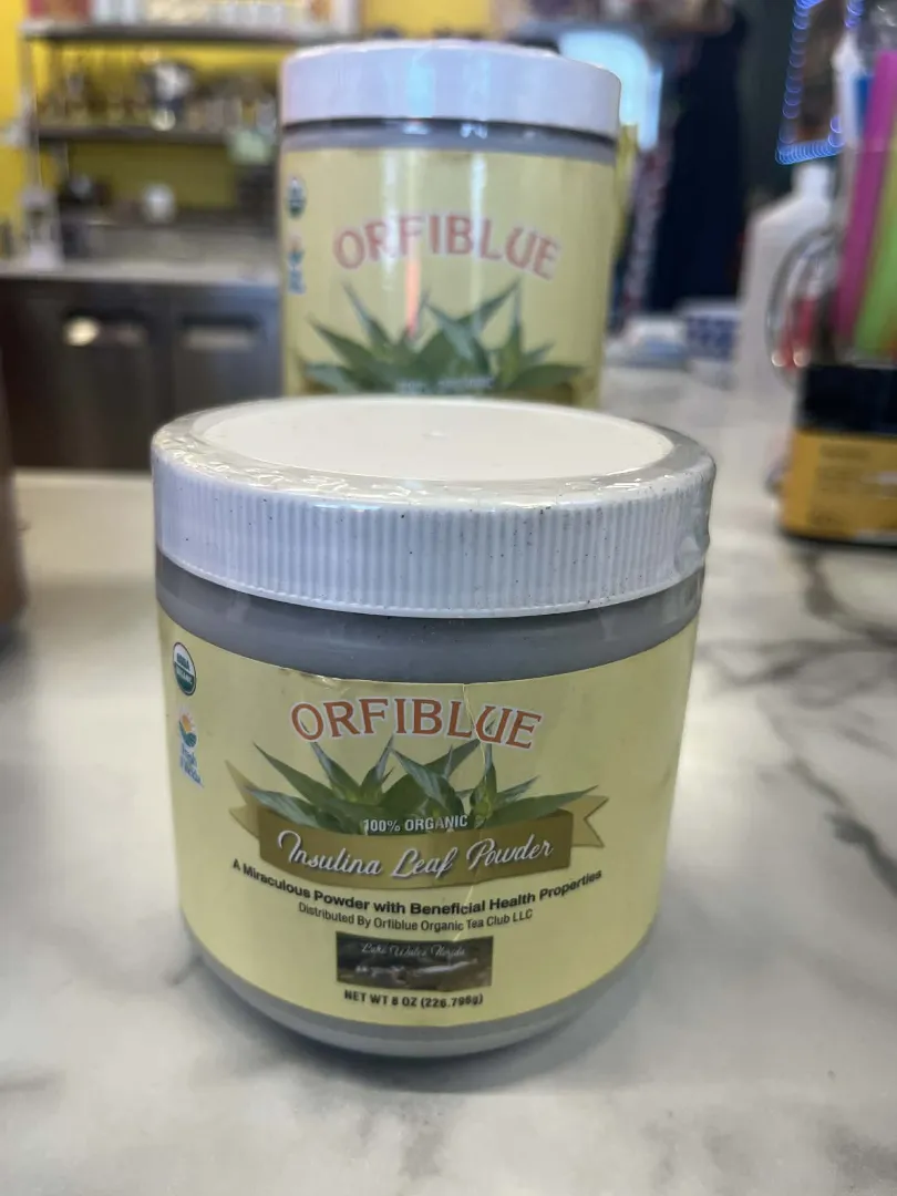 A container of Dr. Schulze's Tea Leaf Powder is displayed on a countertop, with another container of the same vegan-friendly product visible in the background.