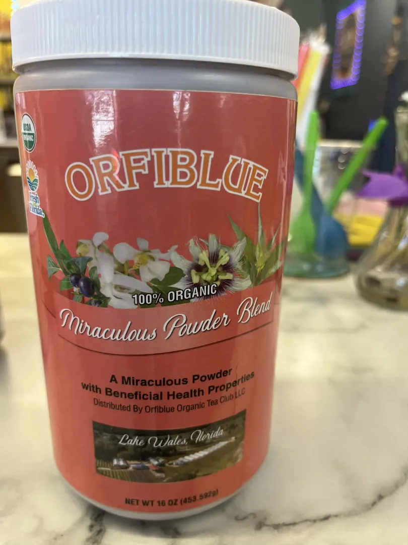 A container labeled "Dr. Schulze's Tea Leaf Powder," 16 oz, 100% organic and vegan, sits on a countertop with blurred background items.